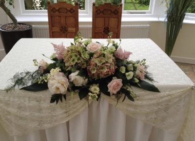 Wedding Table Arrangement. A graceful floral centrepiece featuring soft pink and cream blooms with lush greenery, perfect for dressing your wedding table.
